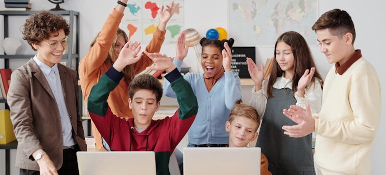 A diverse group of excited students and a teacher celebrate around laptops in a classroom, reflecting the joy of learning and the benefits of living in Shavano Park.