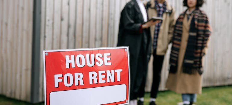 People standing next to the sign house for rent 
