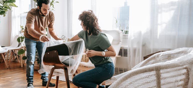 A couple using packing supplies for moving furniture to protect chairs