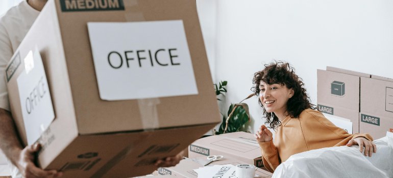 Woman smiling while surrounded by labeled moving boxes during a home office move in Converse.