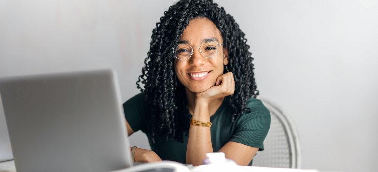 Smiling young woman sitting at a desk with a laptop, appearing confident and ready to work.