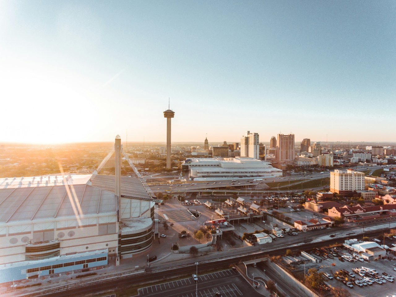 Aerial view of downtown San Antonio at sunrise, featuring the Tower of the Americas and surrounding buildings.
