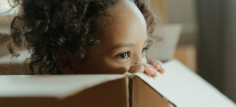 Young child peeking out of a moving box, capturing the playful side of moving with kids to Olmos Park.