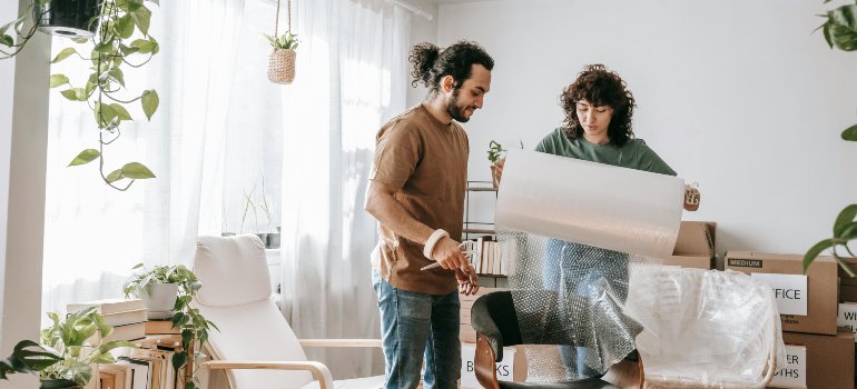 Couple wrapping furniture with bubble wrap while preparing for a home office move in Converse.