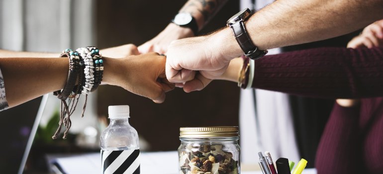 Close-up of a group of coworkers giving a fist bump over a work desk with office supplies and snacks.