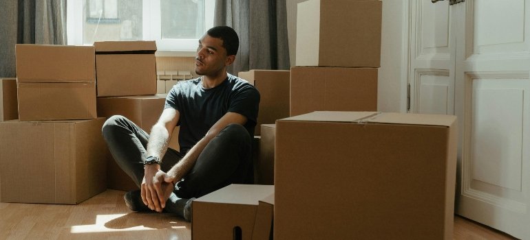Man sitting among packed boxes, reflecting during a move, part of a packing supplies checklist for an office relocation.