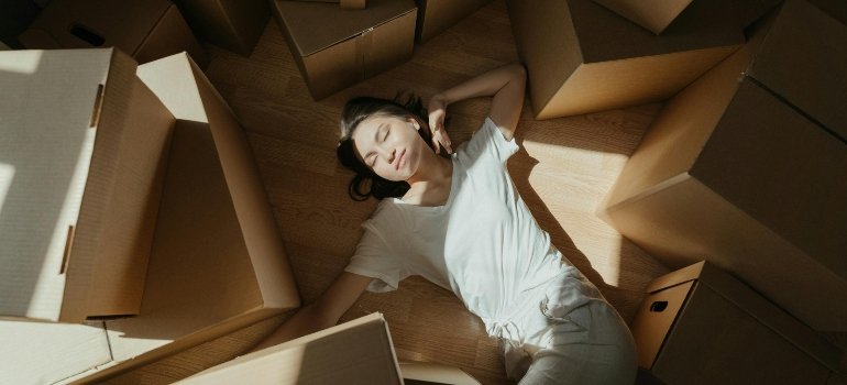 Young woman in white shirt relaxing on the floor surrounded by cardboard boxes.