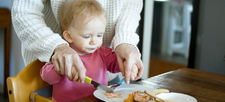 Woman in White Sweater Helping Baby Cut Food
