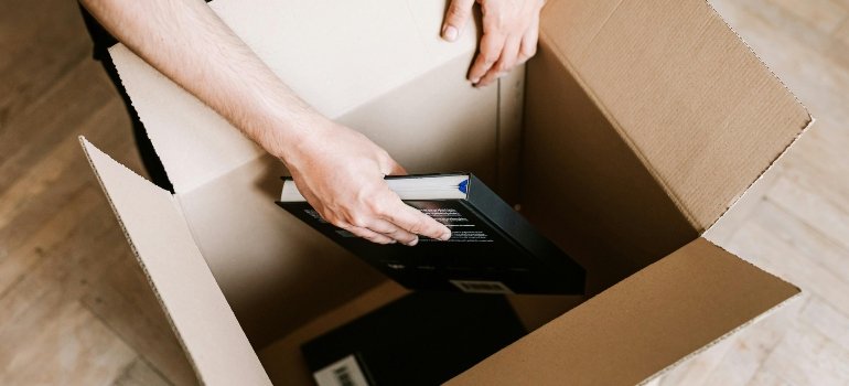Hands placing a hardcover book inside an open moving box.