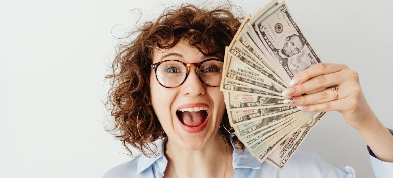 Happy woman in a blue long sleeve blouse holding money, showing the savings when you relocate to a no-income-tax state.