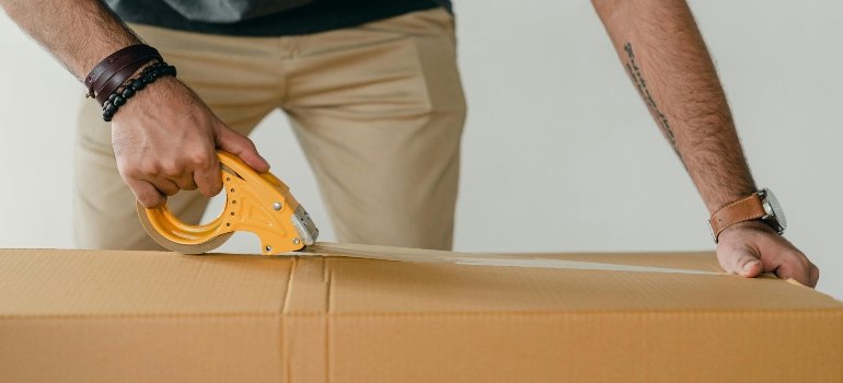 Close-up of a person sealing a cardboard box with packing tape.