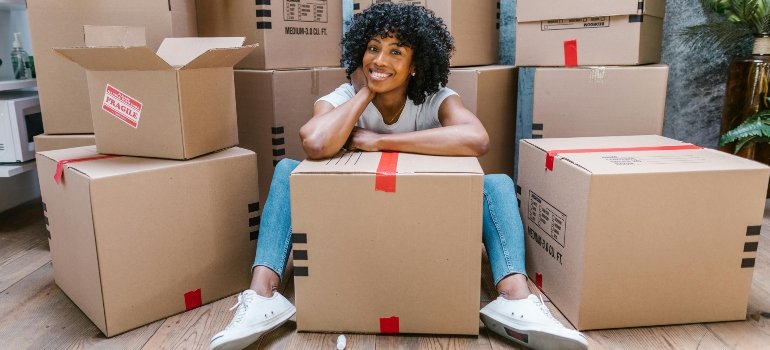 A happy woman sitting on the floor surrounded by boxes, preparing to relocate to a no-income-tax state.