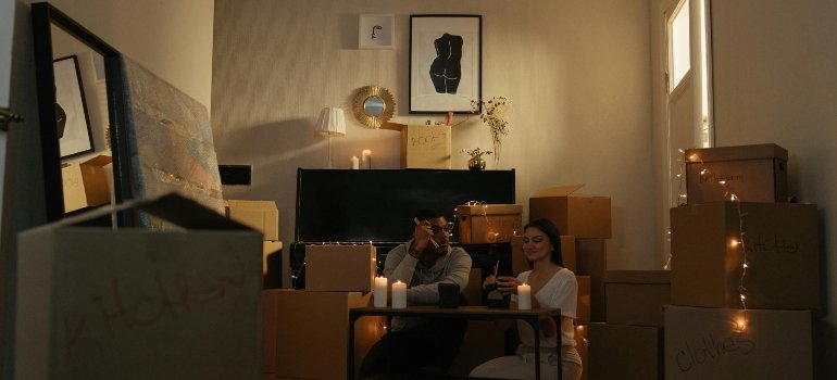 Couple sitting on the floor eating dinner with candles among moving boxes in their new home.