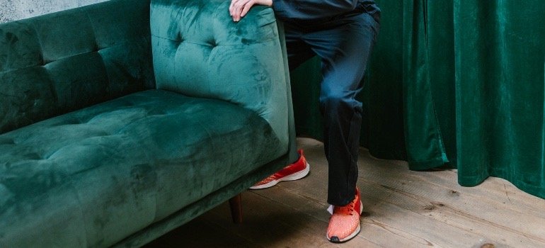 Man carrying green sofa, with bent knees