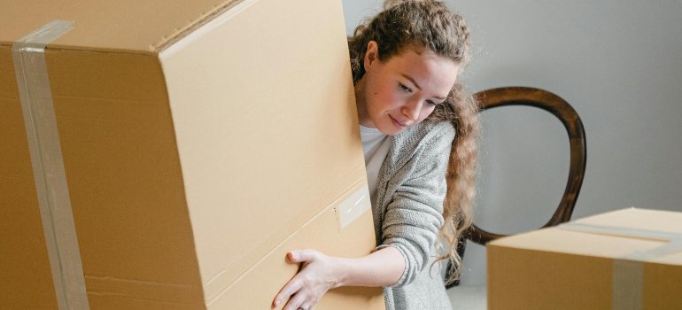 A woman holds a large box in her hands, thinking about tips for moving oversized furniture through narrow hallways.