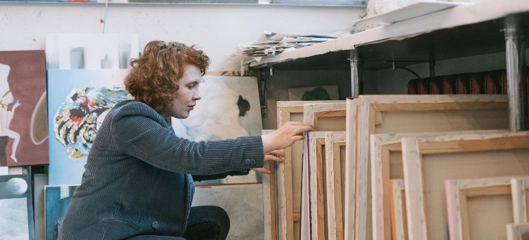 A woman looking through canvases under the table, showing how to pack pictures and paintings when moving