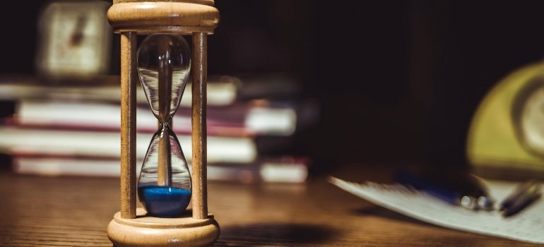 Wooden hourglass with blue sand on a desk, symbolizing preparation and the importance of timing before moving.