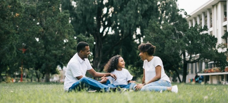 Happy family sitting on grass near their new home, sharing quality time in a peaceful neighborhood.