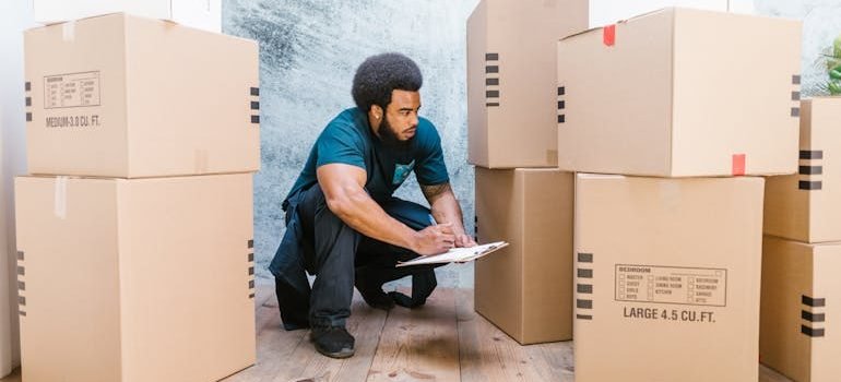 A bearded man crouching and inspecting cardboard boxes while preparing for a move with professional movers in Spring Branch.
