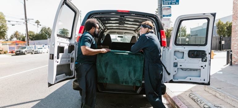 Two professional movers in Spring Branch carefully placing a green velvet box into the back of a moving van during a residential move.