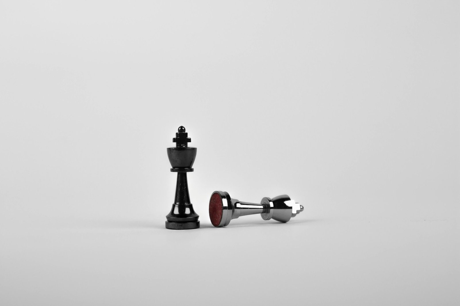 Black king chess piece standing upright beside a fallen silver king on a white surface, symbolizing victory and defeat in a chess match.