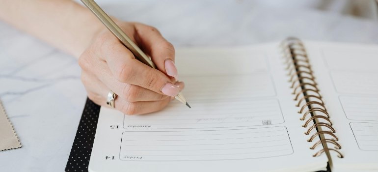 Hand Holding Pencil over Spiral Notebook
