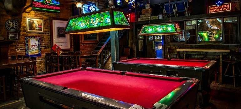 Brown and red billiards tables with green lamps arranged in a game room, relocated by expert pool table movers San Antonio.