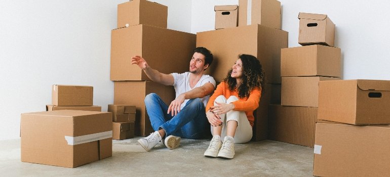 Man and Woman Sitting on Floor Beside Pile of Boxes