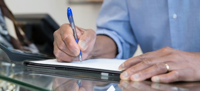 Close-up of man writing utilities setup checklist when moving from Converse to Helotes on paper