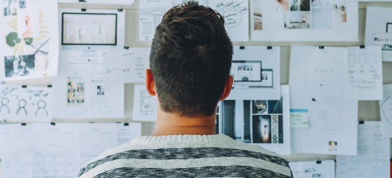 Man Wearing Black and White Stripe Shirt Looking at White Printer Papers on the Wall trying to avoid delays when moving from Cibolo to Uvalde